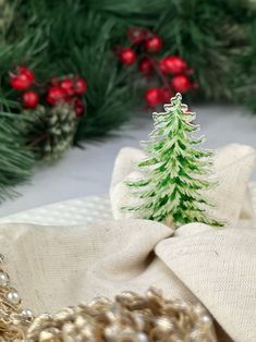 a small green christmas tree sitting on top of a white cloth covered table next to evergreen branches