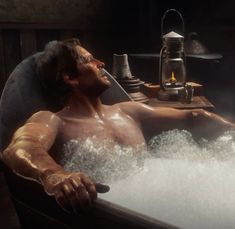 a man laying in a bathtub with foam on the floor and steam coming out of it