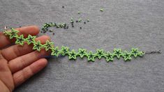 someone is making beaded jewelry with green beads and silver chains on a gray surface