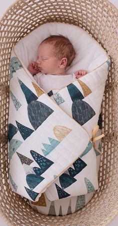 a baby is sleeping in a basket with a pillow on it's back and the cover has trees printed on it