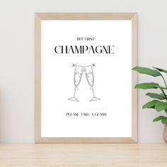 a framed poster with two champagne glasses on it, next to a potted plant