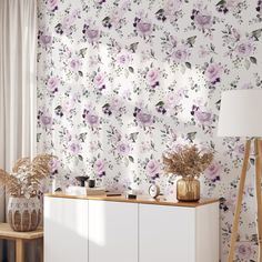 a room with floral wallpaper and white cabinet next to a lamp on a table