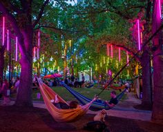 two people laying in hammocks under trees with colorful lights hanging from the branches