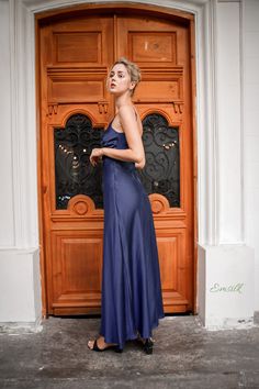 a woman standing in front of a wooden door wearing a blue dress and black heels