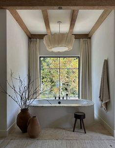 a bath tub sitting under a large window next to a wooden table with two vases on it