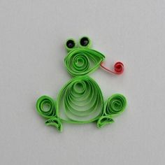 a green frog brooch sitting on top of a white table next to a red thread