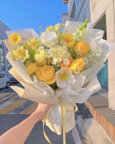 a person holding a bouquet of yellow and white flowers in their hand on the street