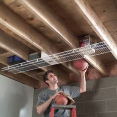 a man holding a basketball in his hand while standing on a ladder under a shelf