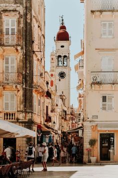 people are walking around in an old european city with tall buildings and a clock tower