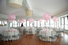 a room filled with lots of tables covered in pink and white balloons next to tall windows