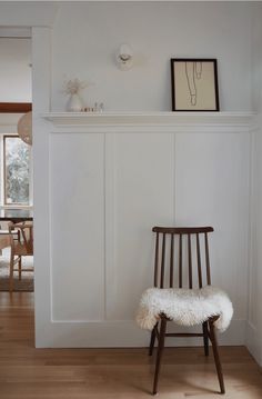 a wooden chair sitting in front of a white wall with a shelf on top of it