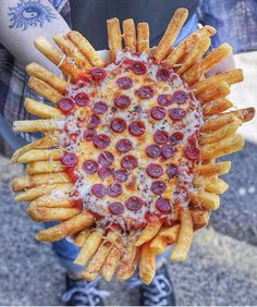 a person holding up a pizza and french fries in their hand with the toppings on it