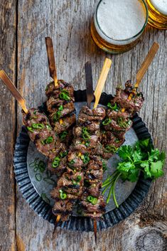 skewers of meat and vegetables on a plate next to two glasses of beer