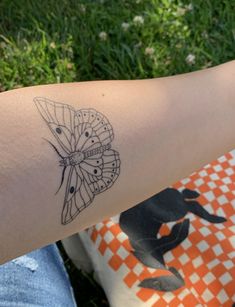 a woman's arm with a butterfly tattoo on it, sitting in the grass