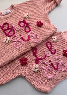 two knitted sweaters with flowers and the words baby love written on them are laying next to each other