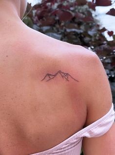 the back of a woman's shoulder with a small mountain tattoo on her left shoulder