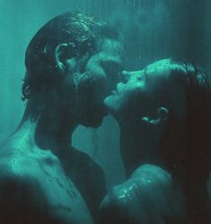 two people in the water kissing each other with their faces covered by blue light from below