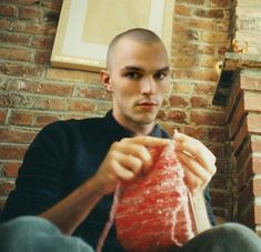 a man sitting on the floor with a knitted item in his hand and wearing a hat