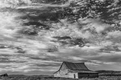 black and white photograph of an old barn in the middle of nowhere with clouds overhead