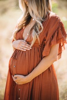 a pregnant woman in an orange dress poses for the camera with her hands on her stomach