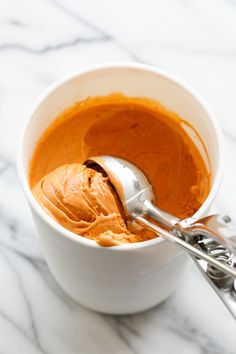 a white bowl filled with peanut butter and a spoon next to it on a marble surface