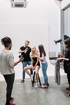 a group of people standing around each other in front of a white wall and camera equipment