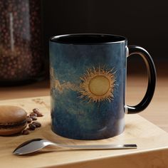 a coffee mug sitting on top of a wooden table next to a spoon and cookie