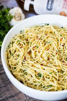 a white bowl filled with spaghetti on top of a wooden table next to garlic and parsley