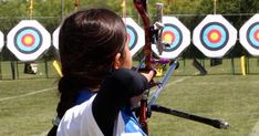 a woman is holding a bow and aiming it at the target in an archery range