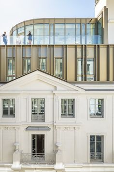 two people standing on the roof of a large white building with glass balconies