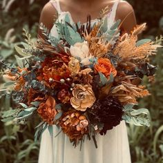 a woman in a white dress holding a large bouquet of flowers and greenery on her arm