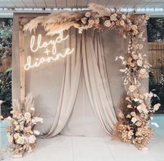 a wedding arch with flowers and feathers on the top is lit up by a neon sign