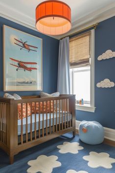 a baby's room with blue walls and white clouds on the ceiling, an airplane print hangs above the crib