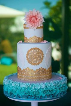 a three tiered cake with blue and gold decorations on the top, sitting on a table