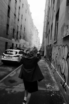 black and white photograph of woman walking down the street in front of graffiti covered buildings