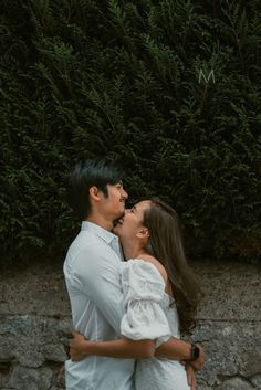 a man and woman standing next to each other in front of a wall with trees