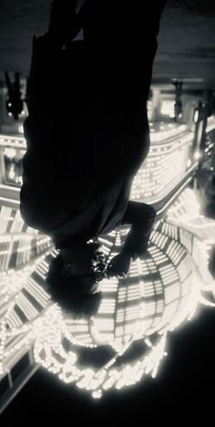 a black and white photo of a person standing in front of a building with lights on it