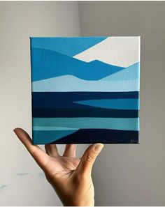 a hand holding up a small blue and white painting