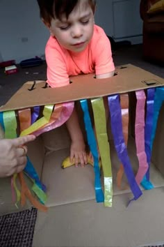 a young child sitting in a cardboard box with streamers on the floor next to it