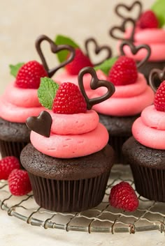 chocolate cupcakes with pink frosting and raspberries on top are sitting on a wire rack