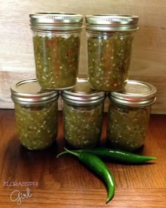 six jars filled with pickles sitting on top of a wooden table next to a green pepper