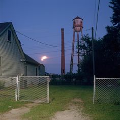 an old water tower is in the distance behind a chain link fence and house at night