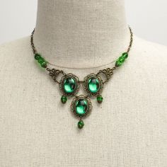 Marquesa Questa jeweled Renaissance necklace in antique bronze metals with emerald green gems Some jewelry was simply made to turn heads. Attract the wandering eye of a nobleman or even a prince with an enticing accessory. Slip on this Marquesa Questa jeweled Renaissance necklace and revel in the stares and praise.This jaw-dropping necklace features three brilliant oval emerald green gems, each mounted in antique bronze. Faceted emerald green crystals capped in the same bronze filigree hang from Jeweled Antique Gold Brass Jewelry, Victorian Style Metal Jewelry With Jewels, Ornate Green Jewelry With Jewels, Antique Green Jewelry For Gifts, Antique Green Jewelry For Gift, Green Brass Jewelry As Gift, Green Brass Jewelry For Gifts, Green Brass Jewelry For Gift, Green Vintage Copper Jewelry