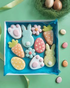 some decorated cookies in a blue box on a green table next to eggs and flowers