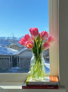 pink tulips sit in a vase on a window sill next to books