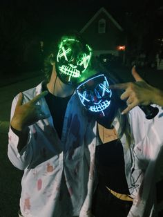 two people wearing neon masks and pointing at the camera with their hands in front of them