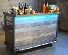 an outdoor bar with drinks on the top and lights at the bottom, in front of a concrete wall