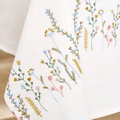 two embroidered tablecloths with flowers on them, one white and the other blue