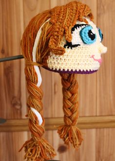 a crocheted hat hanging from a hook on a wooden wall next to a pair of scissors