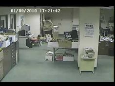 the man is walking through the room in front of the computer desk and other items